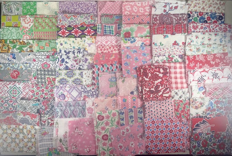 May include: A collection of folded fabric pieces in various patterns and colors. The fabrics feature floral, geometric, and abstract designs in shades of pink, red, green, purple, and white. The arrangement suggests a selection of quilting or crafting materials.
