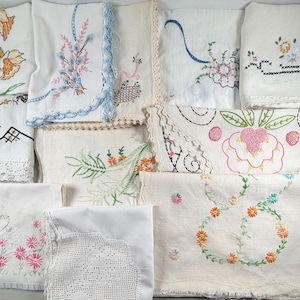 May include: A collection of vintage white linen textiles, each featuring intricate hand-embroidered floral designs in various colors. Some pieces have delicate lace edges, showcasing a variety of needlework styles and patterns. The textiles include napkins and doilies.