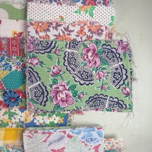 May include: A collection of colorful fabric swatches with floral and patterned designs. The fabrics feature a variety of colors, including green, pink, blue, and yellow. Some swatches have polka dots, while others have intricate floral patterns. The edges of the fabric are frayed.