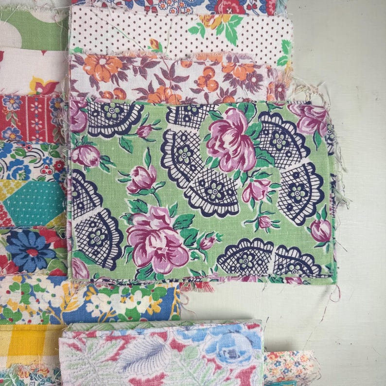 May include: A collection of colorful fabric swatches with floral and patterned designs. The fabrics feature a variety of colors, including green, pink, blue, and yellow. Some swatches have polka dots, while others have intricate floral patterns. The edges of the fabric are frayed.