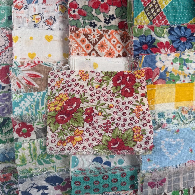 May include: Close-up of a patchwork quilt with a variety of floral and patterned fabric squares. The quilt features red, yellow, and white floral designs, along with other patterns. The edges of the fabric squares are frayed.