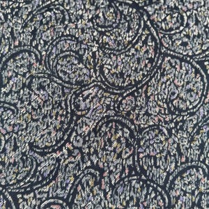Pode incluir: Close-up de um tecido com um padrão paisley. O design apresenta motivos em forma de lágrima em espiral em preto, cinza e toques de roxo, rosa e amarelo. O fundo é azul marinho escuro.