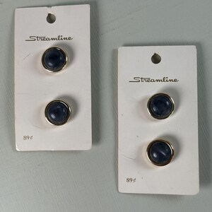 May include: Two sets of Streamline brand buttons. Each set has two dark blue, round buttons with gold-colored rims. The buttons are attached to white cardboard cards. The word "Streamline" is printed on the cards.