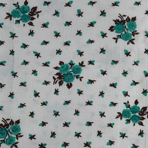 Könnte beinhalten: Weißer Stoff mit einem sich wiederholenden Blumenmuster. Gruppen von türkisfarbenen Rosen mit braunen Stielen und Blättern sind über die Oberfläche verteilt, durchsetzt mit kleineren türkisfarbenen und braunen floralen Akzenten. Der Stoff hat ein leicht strukturiertes Aussehen.