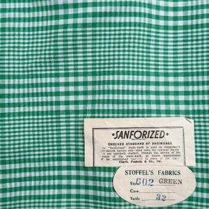 Może przedstawiać: Zielono-biała tkanina w kratę z wzorem w kratę. Etykieta głosi "SANFORIZED" i "STOFFEL'S FABRICS" z numerem stylu 602 i kolorem "GREEN". Tkanina jest sprzedawana w 29,26 metrach.