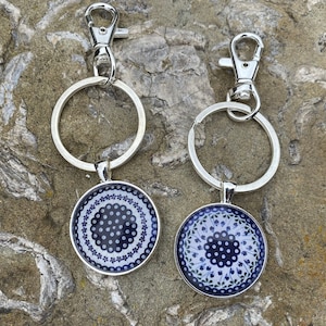 May include: Two silver keychains with blue and white patterned round charms. The charms have a white border and a blue and white floral design.