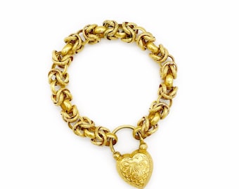 May include: A gold chain bracelet with a heart-shaped padlock charm. The chain is made of interlocking rings and the padlock has an intricate design.