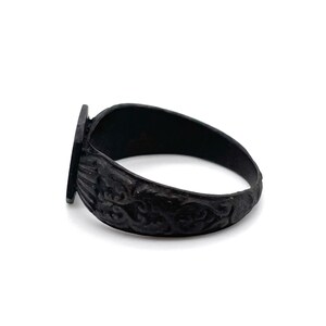May include: A black ring with a rectangular face and ornate, swirling patterns on the band. The ring is made of a dark metal and has a vintage or antique aesthetic. The ring is shown on a white background.