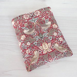 May include: Red fabric book cover with a floral pattern featuring birds and leaves. The fabric has a vintage style.