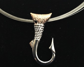 May include: A silver and gold fish hook pendant necklace with a black gemstone eye. The hook is detailed with a textured fish body.