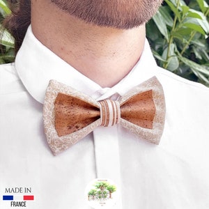 May include: A brown and beige bow tie made of cork with a white patterned design. The bow tie is tied around a white shirt collar. The text "MADE IN FRANCE" is visible in the lower left corner of the image.