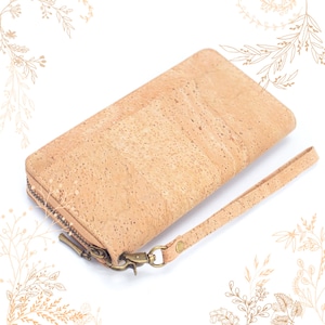 May include: A light brown cork wallet with a zip closure and a wrist strap. The wallet has a textured surface and a bronze-coloured zip and hardware. The wrist strap is attached with a bronze-coloured clasp.