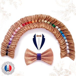 May include: A collection of cork bow ties in various colours, arranged in a semi-circle. A single cork bow tie with a navy blue ribbon is in the centre. The bow ties are made in France, as indicated by the label.