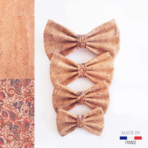 May include: Four cork bow ties in different sizes, with a paisley pattern on the center band. The bow ties are arranged in a vertical stack, with the largest at the top and the smallest at the bottom. The bow ties are made of natural cork and have a light brown color. The text "MADE IN FRANCE" is visible at the bottom of the image.