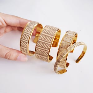 May include: Four gold bangle bracelets with a wood-like pattern. The bracelets are stacked on top of each other.