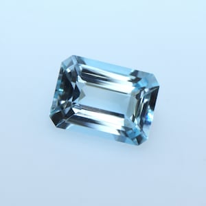 May include: A light blue aquamarine gemstone with a rectangular emerald cut.