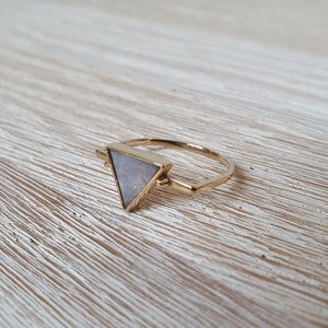 Könnte beinhalten: Ein goldener Ring mit einem dreieckigen Stein. Der Stein ist hellgrau mit einem glitzernden Finish.