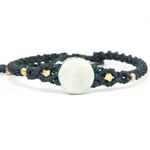 Könnte beinhalten: Ein dunkelgrünes geflochtenes Armband mit einer runden, hellgrünen Steinperle und goldenen Akzenten.