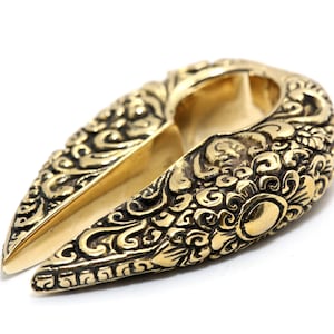 Könnte beinhalten: Ein goldfarbener Ohrring aus Metall mit einem komplizierten floralen Design. Der Ohrring ist an einer Seite offen und hat eine gebogene Form.