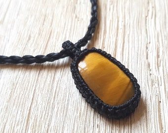 May include: A black cord necklace with a knotted pendant featuring a tiger's eye gemstone.