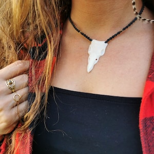 Könnte beinhalten: Nahaufnahme einer Frau, die ein schwarzes Shirt und ein rot-schwarzes kariertes Hemd trägt. Sie trägt eine Halskette mit einem weißen Knochenanhänger und zwei goldene Ringe an ihrem Finger.