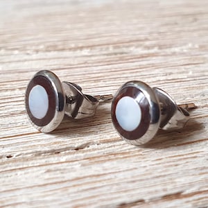 May include: A pair of silver stud earrings with a white mother-of-pearl inlay surrounded by a brown ring.