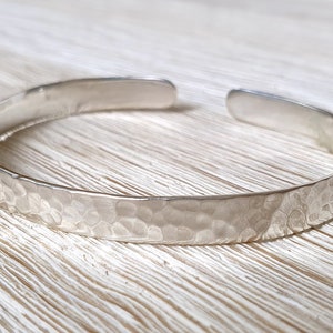 Pode incluir: Um bracelete de prata martelado. O bracelete é feito de uma banda grossa de metal com uma textura martelada. O bracelete é aberto e pode ser ajustado para se ajustar a diferentes tamanhos de pulso.
