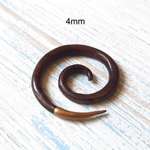 May include: A dark brown wooden spiral ear gauge with a gold-colored tip. The gauge is 4mm in diameter.