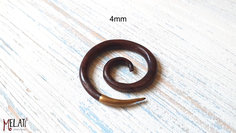 May include: A dark brown wooden spiral ear gauge with a gold-colored tip. The gauge is 4mm in diameter.