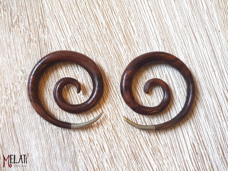 May include: A pair of brown wooden spiral ear gauges with silver accents. The gauges are made of wood and have a spiral design. They are a popular choice for body jewelry.