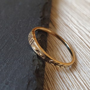 Könnte beinhalten: Ein goldener Ring mit einem zarten, filigranen Design. Der Ring ist dünn und hat eine glatte, polierte Oberfläche.