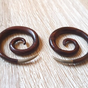 May include: A pair of brown wooden spiral ear gauges with silver accents. The gauges are made of wood and have a spiral design. They are a popular choice for body jewelry.