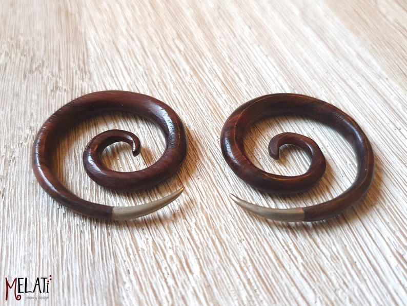 May include: A pair of brown wooden spiral ear gauges with silver accents. The gauges are made of wood and have a spiral design. They are a popular choice for body jewelry.