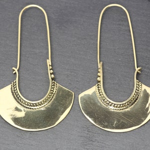 May include: A pair of gold-tone hoop earrings with a decorative design. The earrings are made of metal and have a long, thin drop.