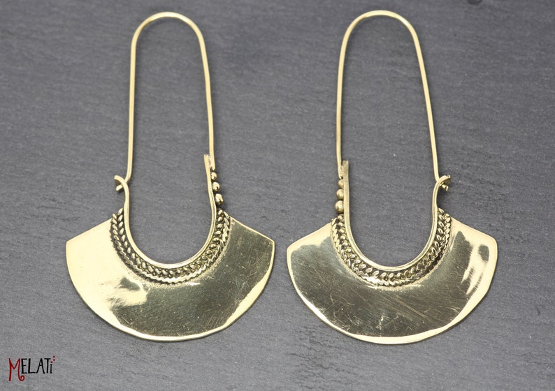 May include: A pair of gold-tone hoop earrings with a decorative design. The earrings are made of metal and have a long, thin drop.