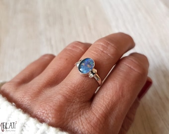 May include: A silver ring featuring an oval blue opal gemstone. The ring has two small silver beads on either side of the stone.