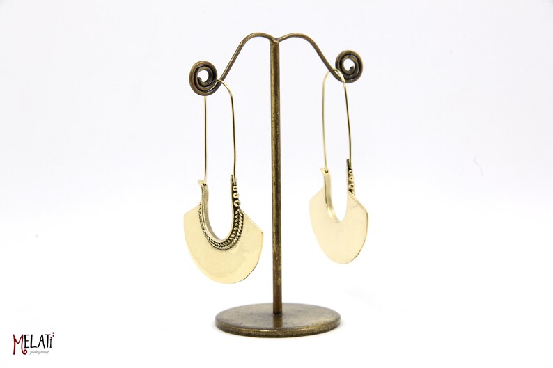 May include: A pair of gold hoop earrings with a decorative design on the bottom half of the hoop. The earrings are hanging from a stand.