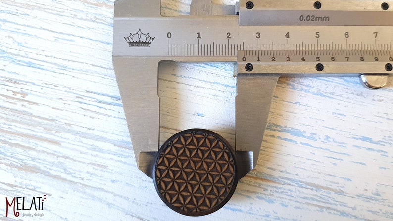 May include: A close-up of a wooden ear gauge with a geometric pattern, measured with calipers to be 2 cm in diameter.