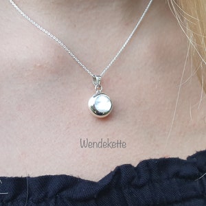 Könnte beinhalten: Eine silberne Halskette mit einem runden Anhänger. Der Anhänger ist glatt und glänzend. Der Text "Wendekette" ist unter dem Anhänger sichtbar.