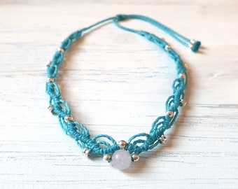 Può includere: Una collana in macramé blu turchese con perline argentate e un ciondolo in pietra bianca.