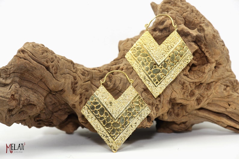 May include: A pair of gold-toned earrings with a geometric, chevron-shaped design. The earrings are made of metal and have a textured surface.