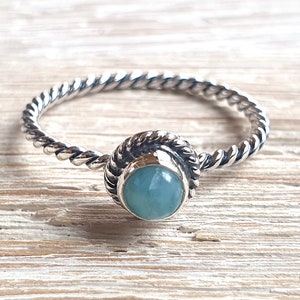 May include: A silver ring with a twisted band and a light blue gemstone set in a silver bezel.