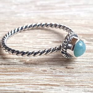 May include: A silver ring with a twisted band and a light blue gemstone set in a silver bezel.
