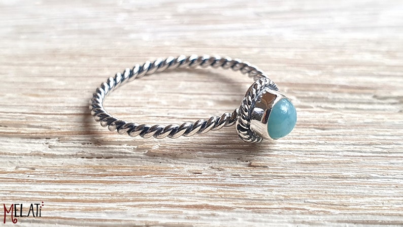 May include: A silver ring with a twisted band and a light blue gemstone set in a silver bezel.