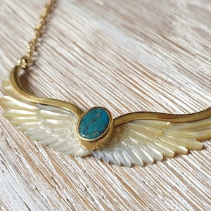 Op de afbeelding: Een gouden ketting met een turquoise steen in een gouden zetting. De hanger is gevormd als een paar vleugels van parelmoer.