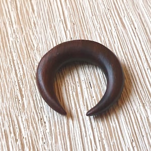 May include: A dark brown wooden crescent moon shaped ear gauge.