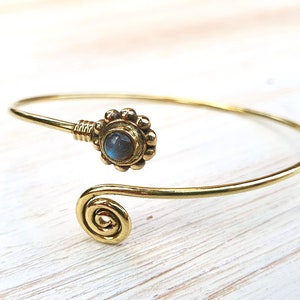 Könnte beinhalten: Ein goldfarbenes Armreif-Armband mit einem Spiraldesign und einem runden, blau-grauen Edelstein, der in einer Messingfassung sitzt.