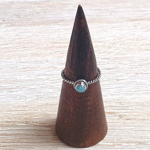 May include: A silver ring with a turquoise stone set in a twisted band. The ring is displayed on a wooden ring holder.