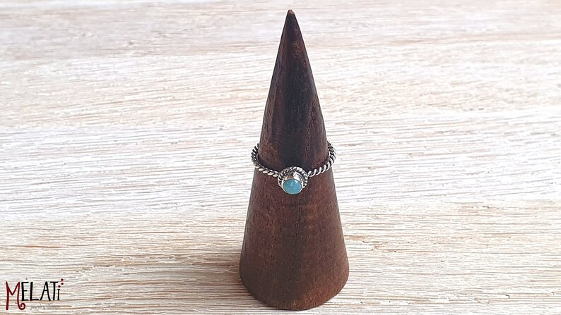 May include: A silver ring with a turquoise stone set in a twisted band. The ring is displayed on a wooden ring holder.