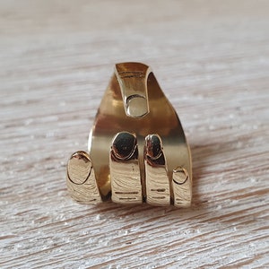 Könnte beinhalten: Ein goldfarbener Ring in Form einer Hand mit vier Fingern. Der Ring ist hinten offen und die Finger sind nach innen gekrümmt.
